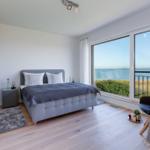 Schlafzimmer mit großem Fenster und Meerblick. Bett, Schrank und Sessel sind vorhanden.