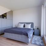 Schlafzimmer mit Bett, Kleiderschrank und großem Fenster mit Blick auf Wasser.