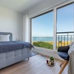 Schlafzimmer mit Blick aufs Meer und Balkon. Bett, Stuhl und Holzboden.