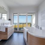 Badezimmer mit Badewanne und Dusche, Blick auf Balkon und Meer.