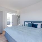 Schlafzimmer mit Bett, Kleiderschrank und Tür zum Balkon.
