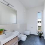Badezimmer mit Waschbecken, Bidet, Toilette und Fenster. Holzunterschrank und Pflanzen.