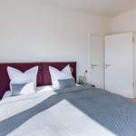 Schlafzimmer mit Bett, Kopfteil und Nachttisch. Blick in das Badezimmer.