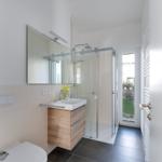 Badezimmer mit Dusche, Waschbecken und Toilette. Durchgang zur Terrasse.