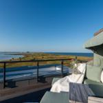 Terrasse mit Sitzgelegenheit und Blick auf Wasser und Grasland.