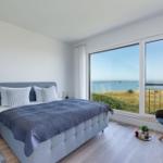 Schlafzimmer mit Blick aufs Meer und Balkon. Bett, Nachttisch und Stuhl.