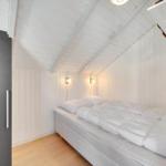 Bedroom with white bed, wooden floor, and white walls under sloped ceiling.