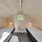 Two beds in a wooden room with window and table.