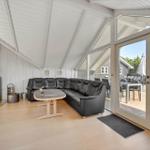 Living area with black sofa, wooden table, and fireplace. Entrance to terrace with table and chairs.