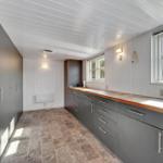 Kitchen with gray cabinets, wooden countertop, and windows. Tile floor and white walls.