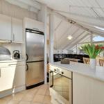 Kitchen with refrigerator, stove, and countertop. Living area with sofa and table in background.
