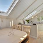 Dining area with round table and chairs under sloped roof with skylight.
