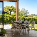 Deck with table and chairs, view of green hedge and tree.