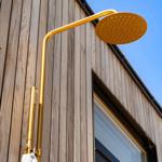 Gold showerhead on wooden wall with window in background.