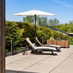 Terrace with lounge chairs and umbrella. Background: green hedge and blue sky.