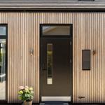 Entrance door with glass panel and wooden facade. A potted plant stands in front.