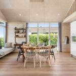 Living kitchen with dining table, sofa, and large windows. Wooden floor and walls.