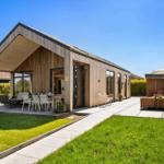 Modern villa with wooden facade, terrace, and garden. Outdoor table, seating, and sunshade.