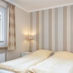 Schlafzimmer mit Doppelbett, Streifenwand, zwei Nachttischen und Fenster mit Vorhang.