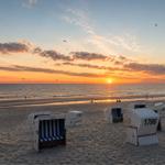 Strand mit Strandkörben und Sonnenuntergang über dem Meer.