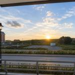 Blick vom Balkon auf Sonnenuntergang, Straße, Parkplatz und Grünfläche.