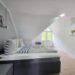Bedroom with sloped ceiling, bed with nautical bedding, window, and desk.