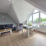 Living and dining area with sofa, table, and windows. Wooden floor and sloped ceiling.