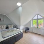 Bedroom with sloped ceiling, anchor-themed bed, armchair, and window view.