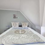 Bedroom with bed, pillows, and blanket featuring anchor motif. A lighthouse picture hangs on the wall.