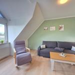 Living room with sofa, chair, table, and window. Green wall, wooden floor.