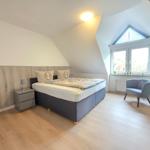 Bedroom with sloped ceiling, bed, nightstand, chair, and window.