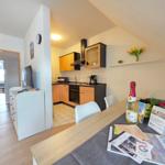 Kitchen with dining area, table with fruit and bottle, TV, and door to living room.