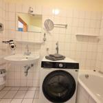 Bathroom with washing machine, bathtub, and mirror on the wall.
