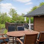 Terrace with wooden table and chairs beside a wooden house. Background: green areas and stone wall.