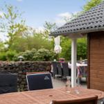 Wooden table with chairs in garden next to wooden house and stone wall.
