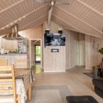 Living area with wooden ceiling, wood stove, TV, and dining table with chairs.