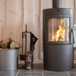 Wood stove with burning fire, next to fireplace tools and firewood in bucket.