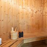 Sauna with wooden walls, bench, and wooden bucket. Two bottles and a wooden bucket are in front.