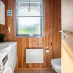 Bathroom with washing machine, toilet, and window with blinds.