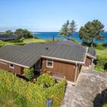 A house with wooden facade and gray roof, surrounded by greenery and overlooking the sea.