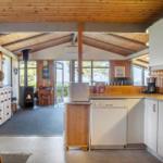 Kitchen with sink and dishwasher, living area with fireplace and wood wall