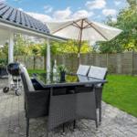 Terrace with table, chairs, umbrella, and grill. Lawn and wooden fence in background.