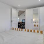 Bedroom with bed, wardrobe, and door to dining area.