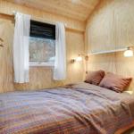 Bedroom with wooden walls, bed, nightstand, and window with curtains.