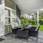 Patio with seating group and table under roof. Lawns and trees in background.