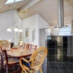 Dining area with wooden table and chairs, kitchen with black tiles and stainless steel hood.