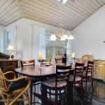 Dining room with round table, chairs, and windows. Wooden ceiling and black tiles.