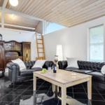 Living room with two black leather sofas, wooden table, and dark floor. Wooden mezzanine area with ladder.