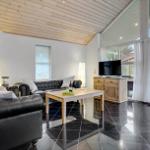 Living room with leather sofa, wooden table, and TV. Black tiles and wooden ceiling.