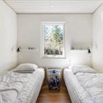 Two beds with white bedding face a window with a view of trees.